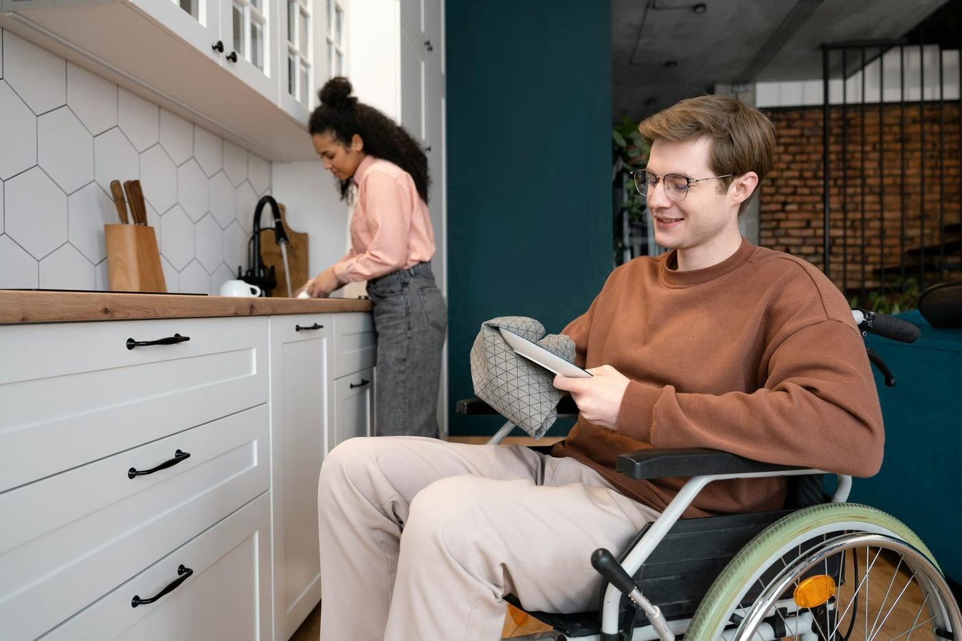Participant reviewing his support plan on a tablet at home while a support worker helps in the kitchen