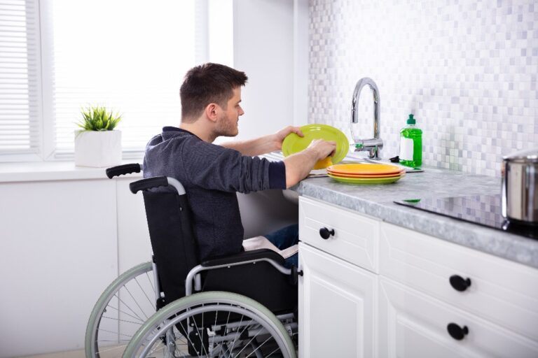 Man in a wheelchair washing dishes independently in his home kitchen